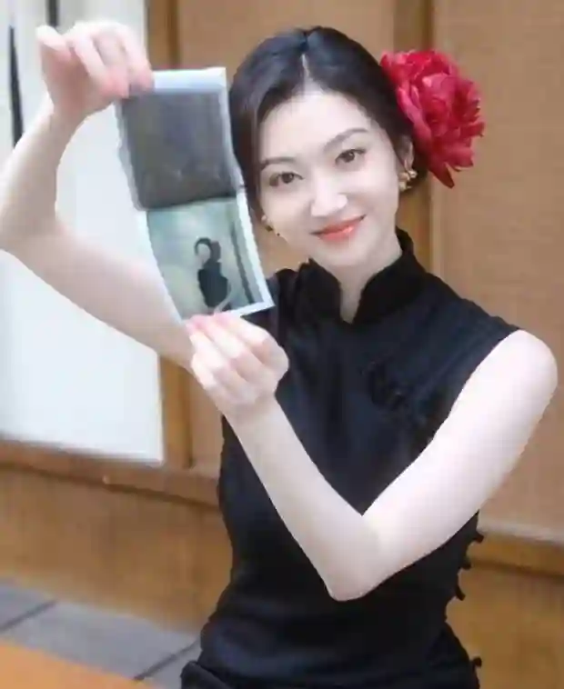 景甜黑色无袖旗袍裙撕拉片，头戴大红花演绎复古明艳风